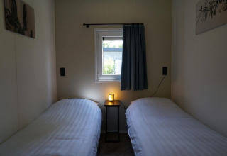 Deux lits simples avec draps blancs, petite table et fenêtre dans Cube la Mer Wellness, Kagerplassen.