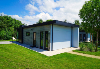 Cube la Mer Wellness lodge at Kagerplassen in the Netherlands surrounded by green lawn and trees on a sunny day.