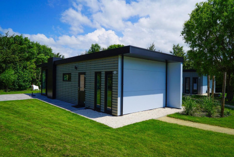 Cube la Mer Wellness lodge aan Kagerplassen, Nederland, met gras en bomen onder een blauwe hemel.