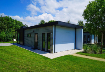 Lodge moderne Cube la Mer Wellness à Kagerplassen, Pays-Bas, entouré de pelouse verte et d’arbres sous le soleil.