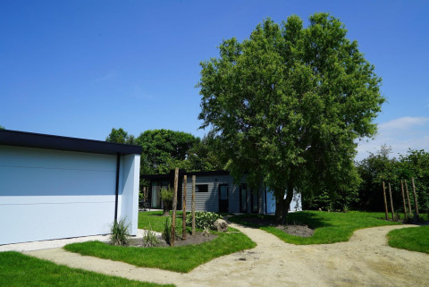 Modern lodge at Cube la Mer Wellness, Kagerplassen in the Netherlands, with green lawn and large tree.