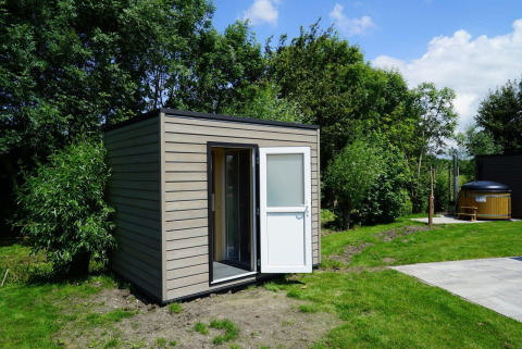 Pequeña cabaña moderna en Cube la Mer Wellness en Kagerplassen, Países Bajos, rodeada de vegetación.