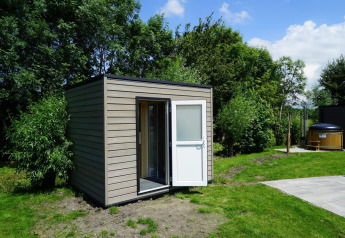 Pequeña cabaña moderna en Cube la Mer Wellness en Kagerplassen, Países Bajos, rodeada de vegetación.