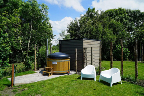 Wellnessbereich im Freien bei Cube la Mer Wellness, Kagerplassen, mit Badefass und weißen Stühlen im Garten.