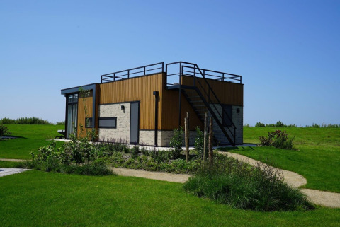 Pavillon lodge moderne à Kagerplassen, Pays-Bas, entouré de pelouse verte et ciel bleu dégagé.