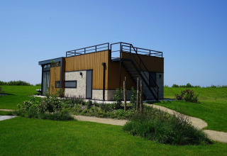 Lodge tipo pabellón moderno en Kagerplassen, Países Bajos, rodeado de césped verde y cielo azul claro.