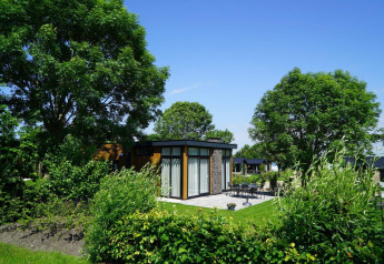 Pabellón lodge moderno en Kagerplassen, Países Bajos, rodeado de árboles, jardín verde y terraza exterior.