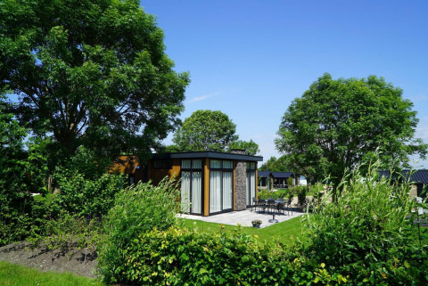 Pabellón lodge moderno en Kagerplassen, Países Bajos, rodeado de árboles, jardín verde y terraza exterior.