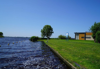 Foto del Pavilion en Kagerplassen, Países Bajos, con césped, agua, un árbol y edificio moderno al fondo.