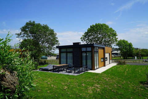 Moderne Pavilion Lodge am Kagerplassen in den Niederlanden mit großer Terrasse, viel Grün und Bäumen.