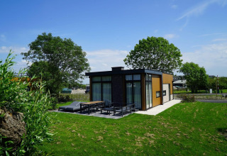 Moderne Pavilion Lodge am Kagerplassen in den Niederlanden mit großer Terrasse, viel Grün und Bäumen.