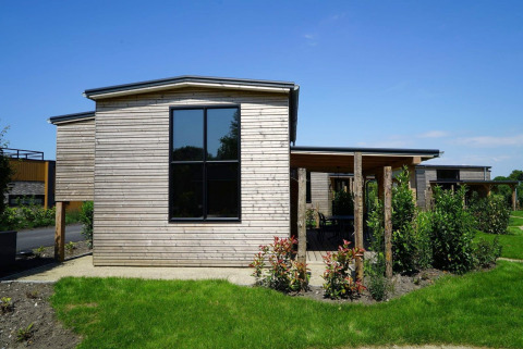 Tiny house moderne en bois avec de grandes fenêtres et un jardin vert sous un ciel bleu clair.