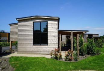 Moderne Tiny House med træbeklædning, store vinduer og grøn have under en klar blå himmel.
