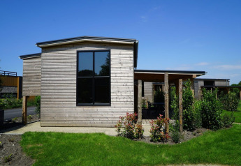 Tiny house moderna de madera con grandes ventanales y jardín verde bajo un cielo azul despejado.