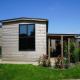 Moderne Tiny House med træbeklædning, store vinduer og grøn have under en klar blå himmel.