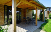 Veranda in legno di una Tiny House a Kagerplassen, Paesi Bassi, con tavolo, sedie e vista sul giardino.