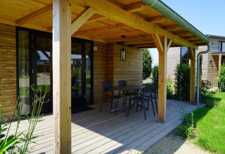 Porche de madera de una Tiny House en Kagerplassen, Países Bajos, con mesa, sillas y vistas al jardín.