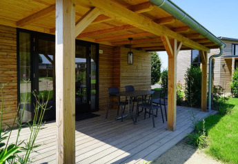 Porche de madera de una Tiny House en Kagerplassen, Países Bajos, con mesa, sillas y vistas al jardín.