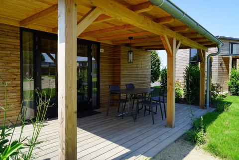 Veranda in legno di una Tiny House a Kagerplassen, Paesi Bassi, con tavolo, sedie e vista sul giardino.