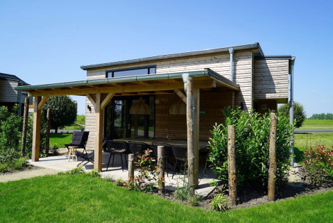 Tiny House aux Kagerplassen aux Pays-Bas, extérieure en bois, terrasse couverte et jardin verdoyant.