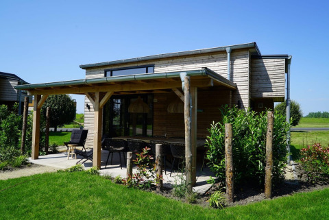 Tiny House ved Kagerplassen i Holland med træfacade, overdækket terrasse og grøn have på en solrig dag.