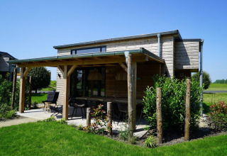 Tiny House ved Kagerplassen i Holland med træfacade, overdækket terrasse og grøn have på en solrig dag.