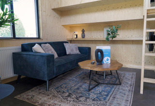 Salon moderne et lumineux dans un Tiny House à Kagerplassen, Pays-Bas, avec canapé bleu et table bois.