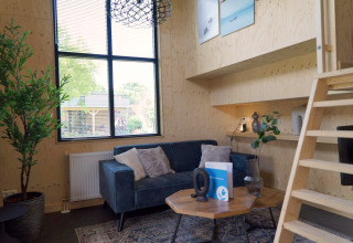 Salon moderne dans un Tiny House à Kagerplassen, Pays-Bas, avec canapé bleu, murs en bois et grande fenêtre.