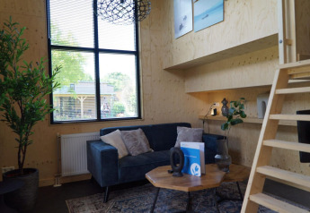 Sala moderna en Tiny House en Kagerplassen, Países Bajos, con sofá azul, paredes de madera y ventana grande.
