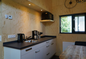 Modern tiny house kitchen at Kagerplassen, Netherlands, featuring wooden walls, coffee maker, and window.