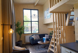 Vue intérieure d’un Tiny House à Kagerplassen, Pays-Bas, avec mezzanine en bois, canapé et grande fenêtre.
