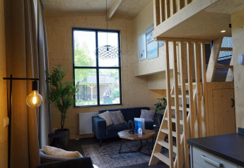 Vista interior de Tiny House en Kagerplassen, Países Bajos, con sofá, altillo de madera y ventana grande.