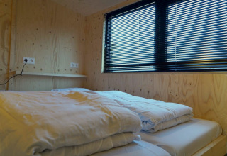Chambre moderne avec murs en bois, lit et grandes fenêtres à stores dans une tiny house aux Pays-Bas.