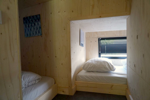 Intérieur d'une tiny house en bois à Kagerplassen, Pays-Bas, avec deux lits et une fenêtre à store.