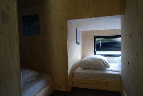 Interior de una pequeña casa de madera en Kagerplassen, Países Bajos, con dos camas y ventana con persiana.
