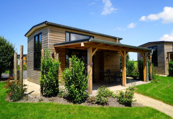 Et lille træhus med veranda og store vinduer, omgivet af grøn have, Tiny House ved Kagerplassen, Holland.