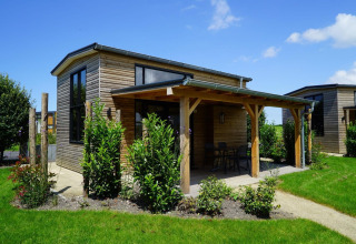 Pequeña casa de madera con terraza cubierta y grandes ventanas en jardín verde, Tiny House at Kagerplassen, Países Bajos.