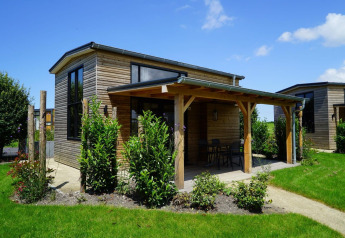 Pequeña casa de madera con terraza cubierta y grandes ventanas en jardín verde, Tiny House at Kagerplassen, Países Bajos.