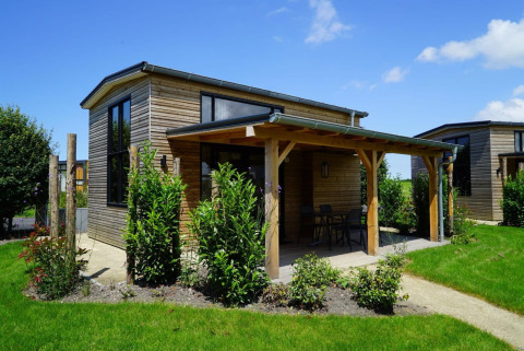 Petite maison en bois avec terrasse couverte et grandes fenêtres dans un jardin, Tiny House à Kagerplassen, Pays-Bas.