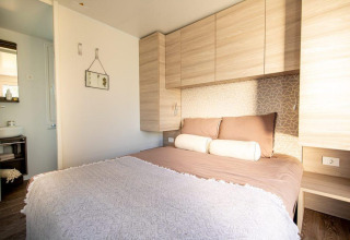 Lichte lodge-slaapkamer met tweepersoonsbed, houten kasten, kussens en zicht op badkamer in de hoek.