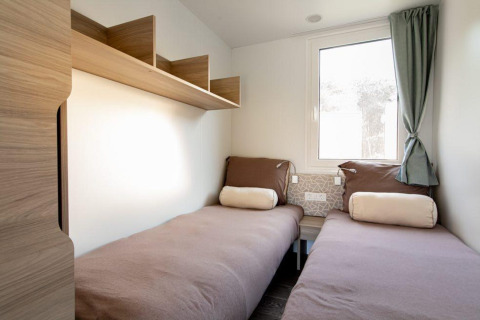 Lichte lodgekamer met twee single bedden, houten schappen, raam met gordijn en neutrale kleuren.