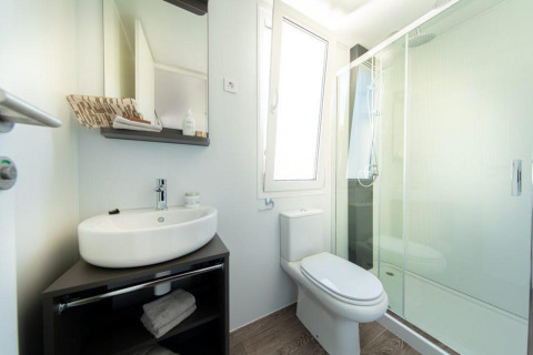 Baño moderno en un lodge con lavabo, inodoro, espejo, ducha de vidrio y una ventana amplia y luminosa.