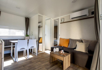 Moderne lodge med stue, spisebord og aircondition, lyst interiør og træmøbler, hyggelig stemning.