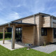 En moderne Tiny House Plus lodge med træbeklædning, overdækket terrasse og grøn græsplæne udenfor.