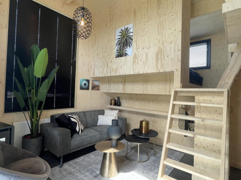 Acogedora sala moderna en Tiny House Plus en De Rijp, Países Bajos, con sofá gris y escalera de madera.