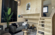 Acogedora sala moderna en Tiny House Plus en De Rijp, Países Bajos, con sofá gris y escalera de madera.