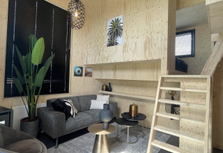 Moderne leefruimte in Tiny House Plus lodge te De Rijp, Nederland, met houten trap en zetel.