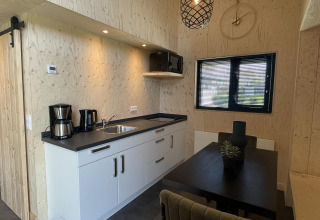 Moderne køkken og spiseområde i Tiny House Plus-lodgen ved De Rijp, Holland, med trævægge og sort interiør.