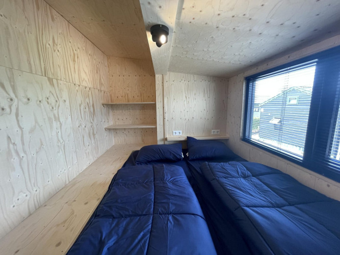 Bedroom at Tiny House Plus in De Rijp, Netherlands, featuring twin beds with navy blue bedding and wooden walls.