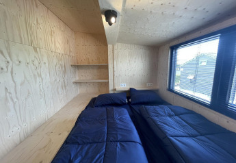 Chambre au Tiny House Plus à De Rijp, Pays-Bas, avec deux lits jumeaux bleu marine et murs en bois clair.